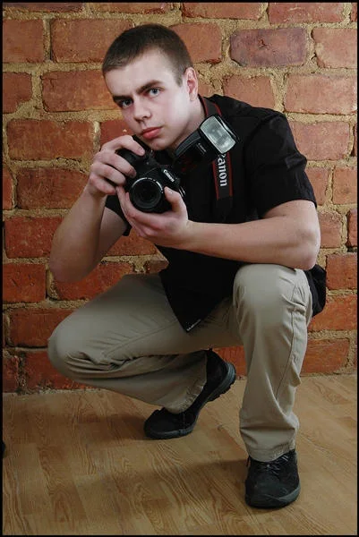 Mateusz Mania z aparatem Canon przy ceglanej ścianie