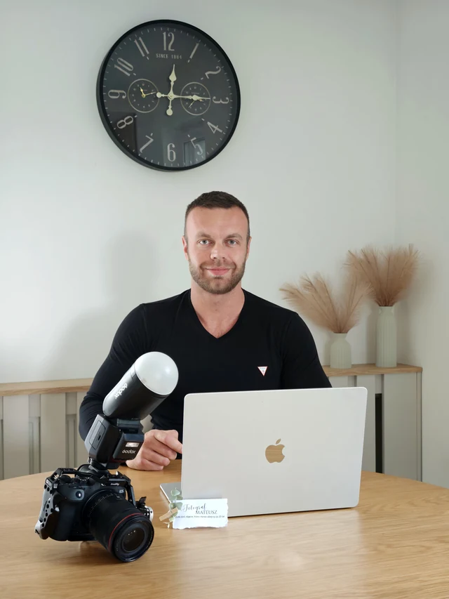 Mateusz Mania przy biurku z aparatem i laptopem