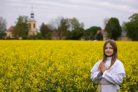 Dziewczynka w stroju komunijnym na tle kwitnącego pola