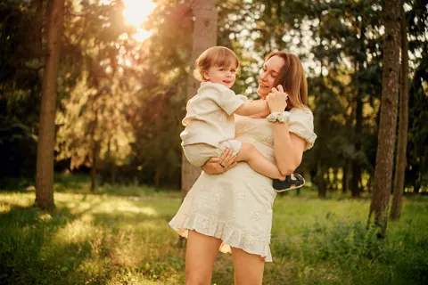 Mama niesie dziecko w słonecznym ogrodzie