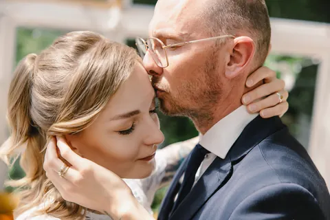 Pan młody całuje pannę młodą w czoło podczas sesji w szklarni